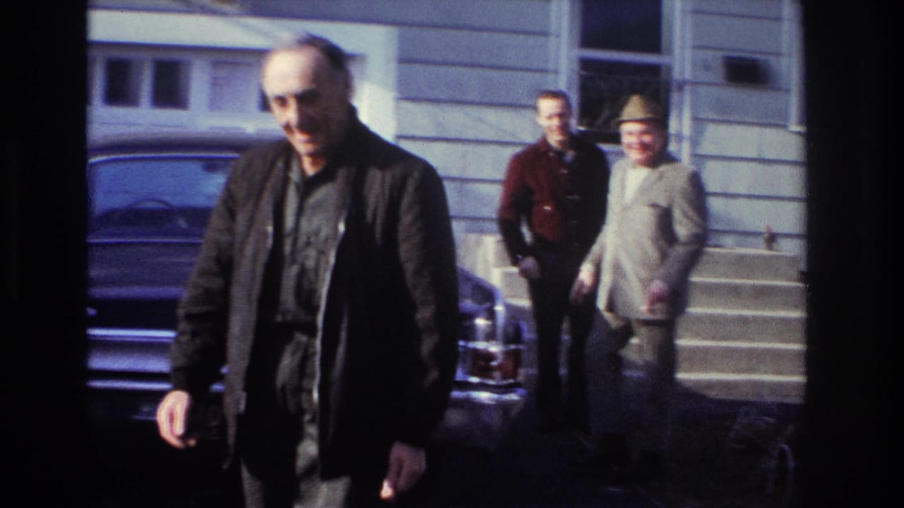 The older man moves closer to the camera, with two adult men behind him near the steps of a Hoboken house in 1966 footage.