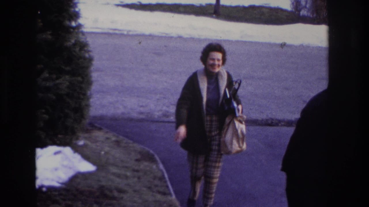 Woman with handbag continues toward the camera near a driveway and parked car edge.