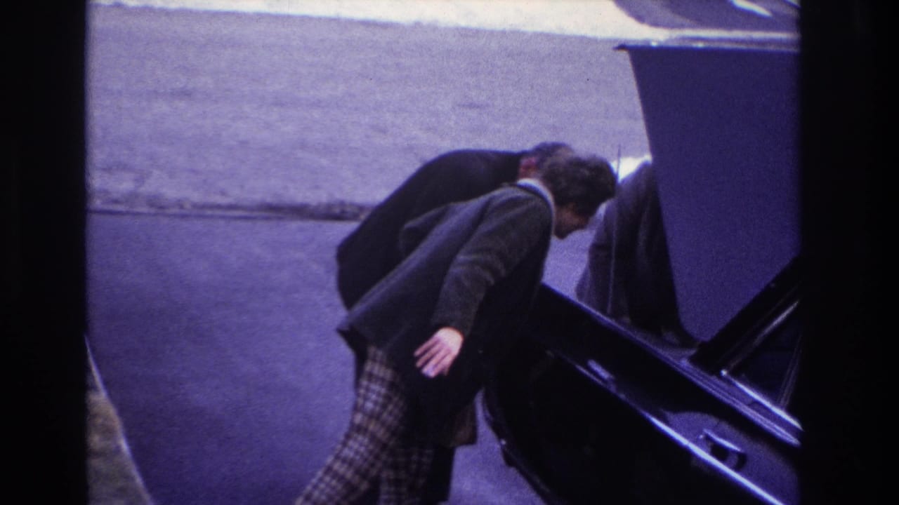 In 1966 Hoboken home-movie footage, a woman in plaid pants stands beside a black car as a man works near the raised hood.