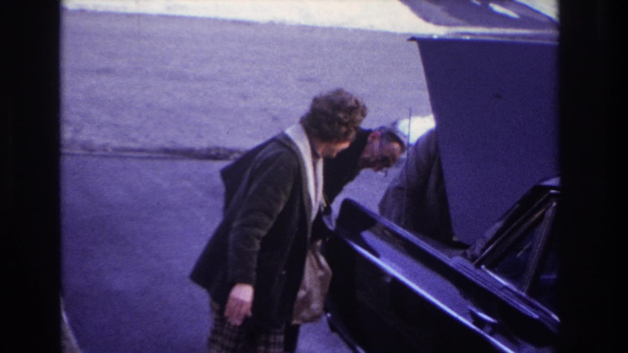 Woman looks toward a man bending into the engine compartment of a black car.