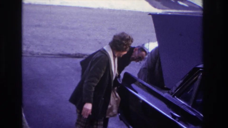 The woman stands near the passenger side of a black car in Hoboken as a man bends into the open hood area.