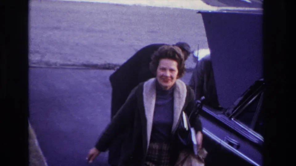 A smiling woman in a dark coat with a light collar faces the camera while the car remains open behind her.