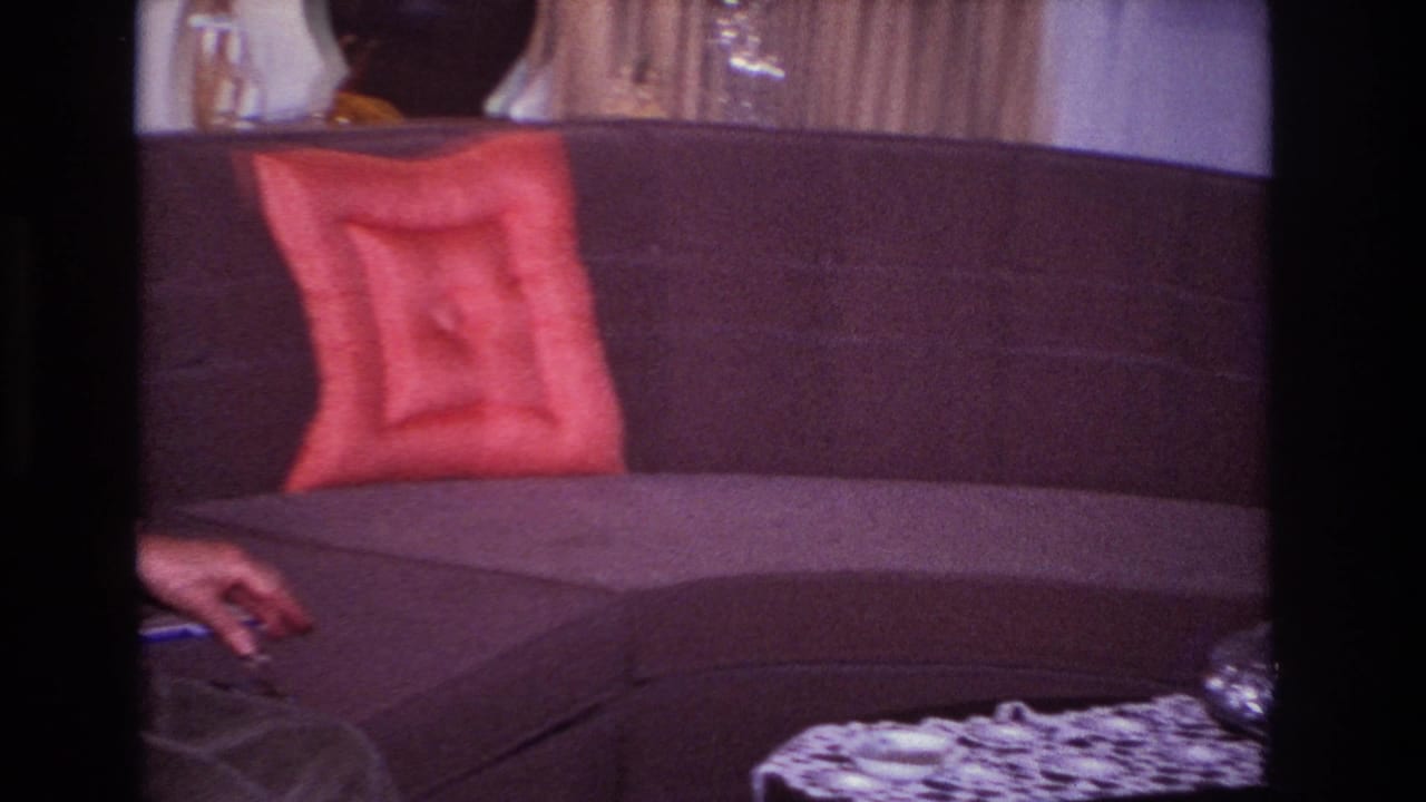 Dark sectional sofa with red pillow, tabletop edge, and part of a seated person's arm.