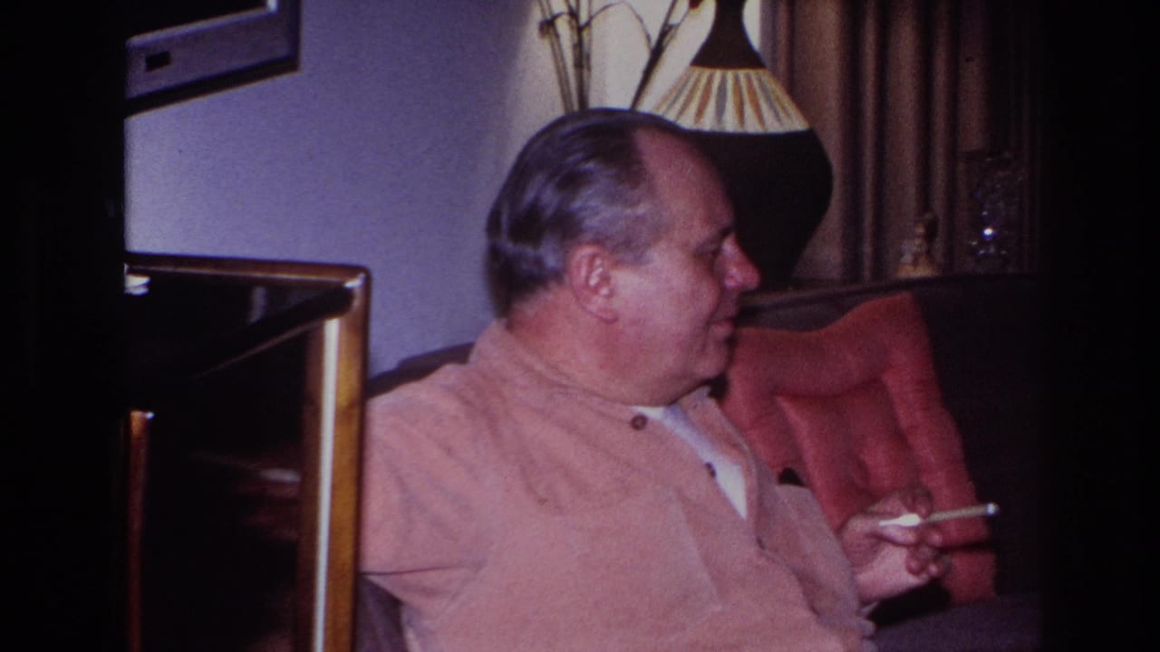 In a 1966 Hoboken home-movie frame, an older man sits in profile in a red chair, holding a cigarette in a dim living room.