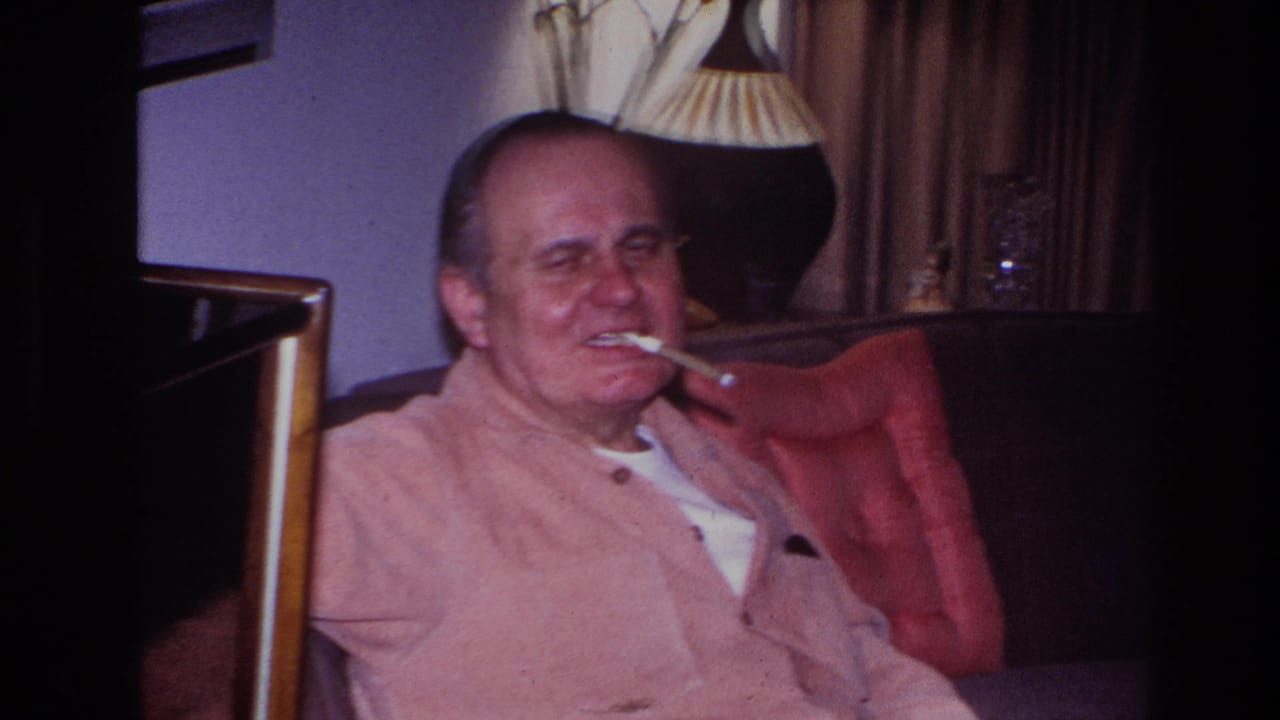 Man reclines on a sofa with smoke held at his mouth.