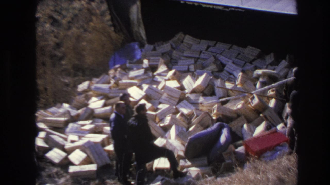Hoboken, New Jersey 1966 frame with men in dark coats gathered around a large pile of dumped boxes on an outdoor slope.
