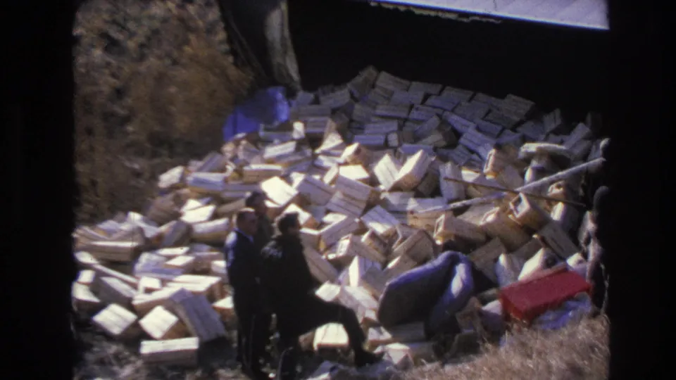 Hoboken, New Jersey 1966 frame with men in dark coats gathered around a large pile of dumped boxes on an outdoor slope.