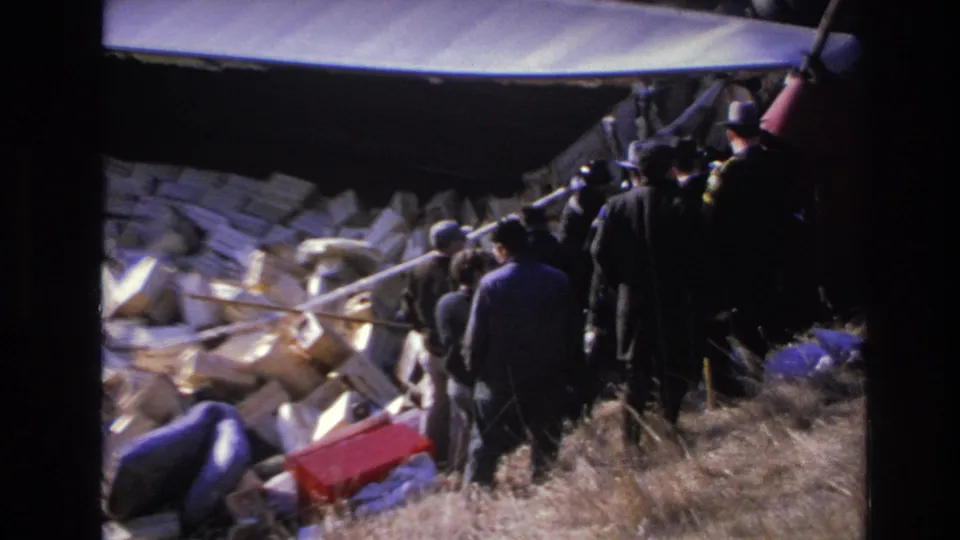 Hoboken, New Jersey 1966 frame showing a larger group of men beside spilled boxes below a dark truck body on a grassy slope.