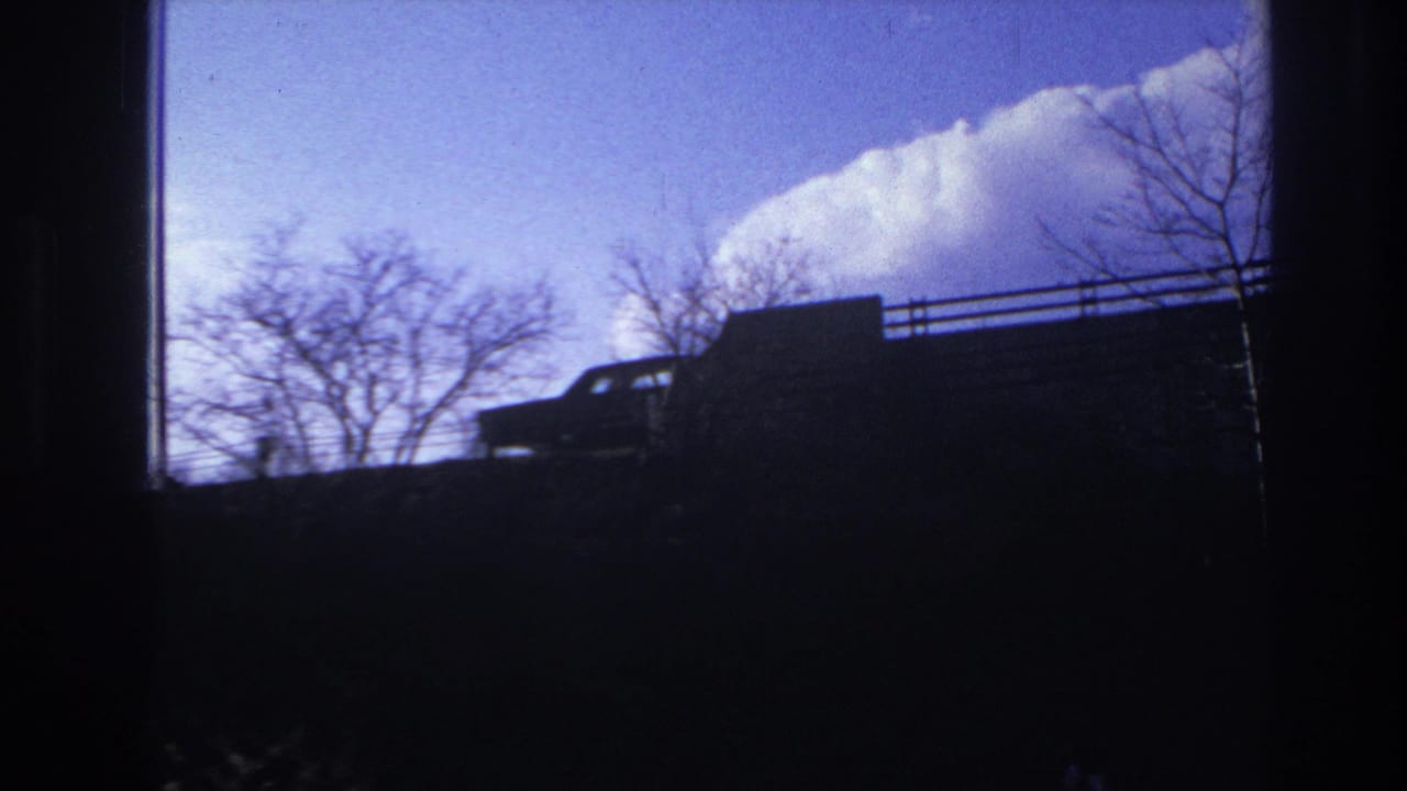 Silhouetted car and bare trees appear along the top of an elevated road against a blue sky.