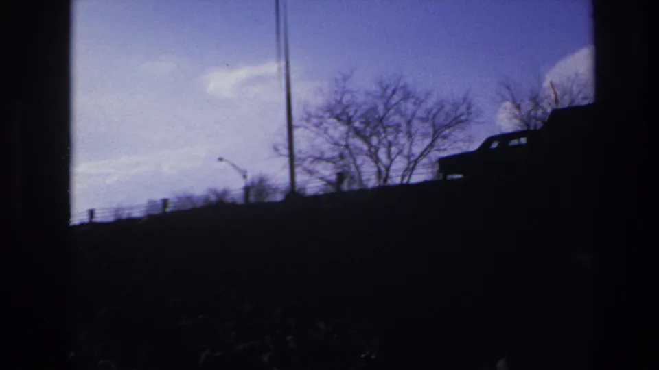 1966 Hoboken low-angle frame showing a silhouetted car near the edge of the elevated road, with trees and a tall pole against the sky.