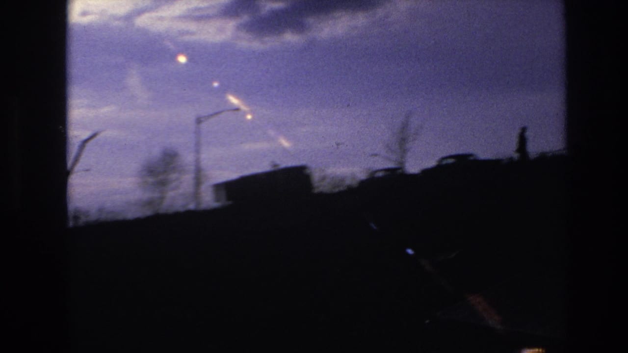 Dark ridge with streetlights, a vehicle shape, and silhouetted figures against a twilight sky.