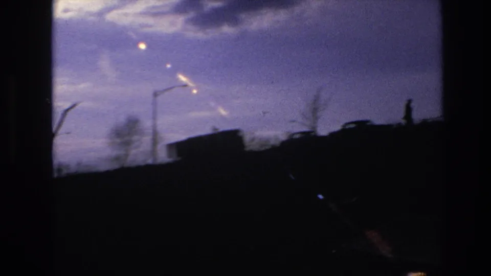 1966 Hoboken-area home-movie frame with streetlights, a vehicle shape, and small silhouetted people along a dark ridge at twilight.