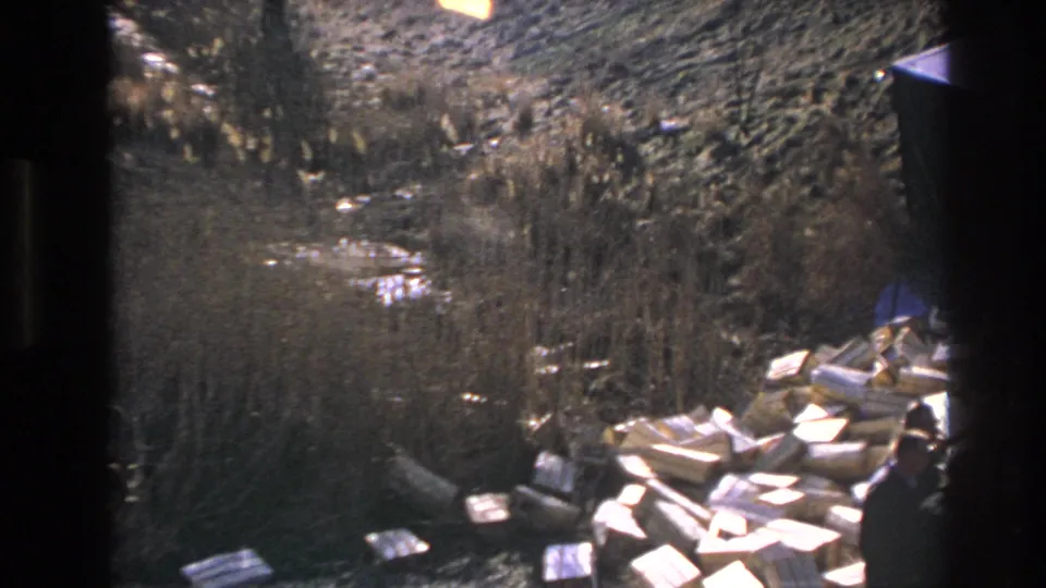 1966 Hoboken-area 8mm frame showing rough sunlit ground with puddles, brush, and scattered wood boards or crate fragments.