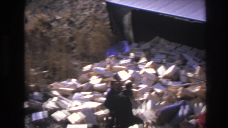 1966 Hoboken home-movie frame looking down on a man and scattered white blocks near a dark vehicle side.