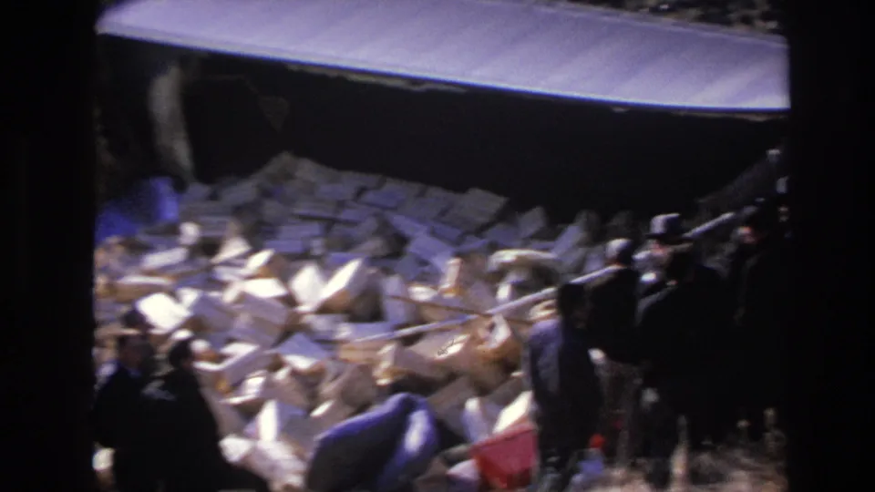 1966 Hoboken frame showing men gathered at the right of a block pile beside a truck or trailer in an outdoor area.
