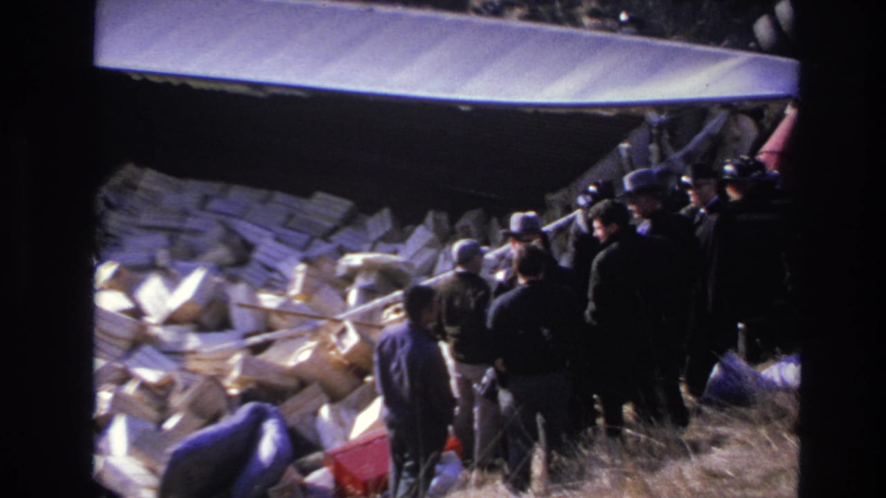 1966 Hoboken 8mm frame showing men gathered beside overturned red helicopter wreckage, white debris, and dry grass on a hillside.