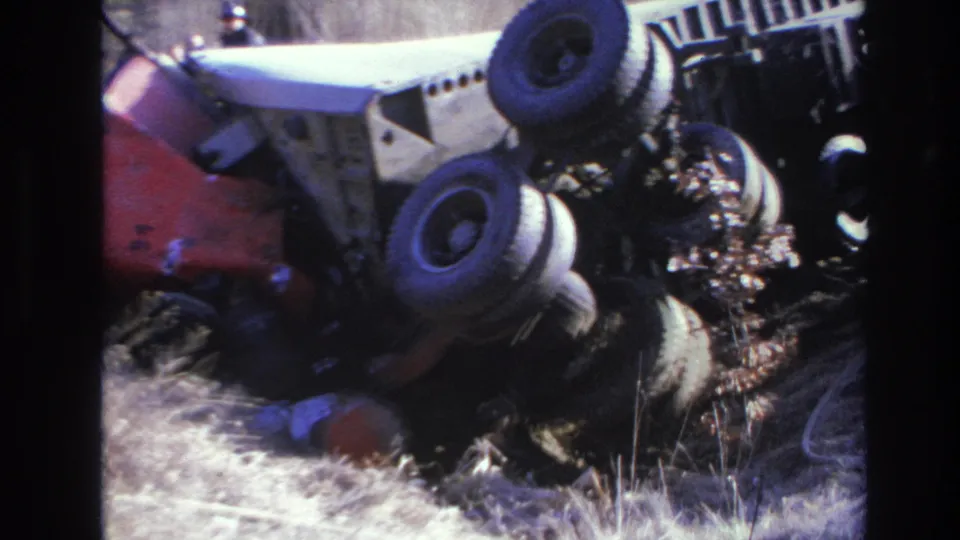 Final frame shows the overturned truck from close range, with wheels above the ditch and indistinct people near the edge of the scene.