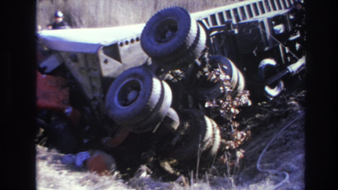 1966 Hoboken-area 8mm frame showing a large truck rolled onto its side in dry grass, with exposed wheels and scattered brush.