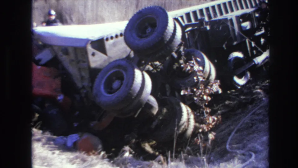 1966 Hoboken-area 8mm frame showing a large truck rolled onto its side in dry grass, with exposed wheels and scattered brush.