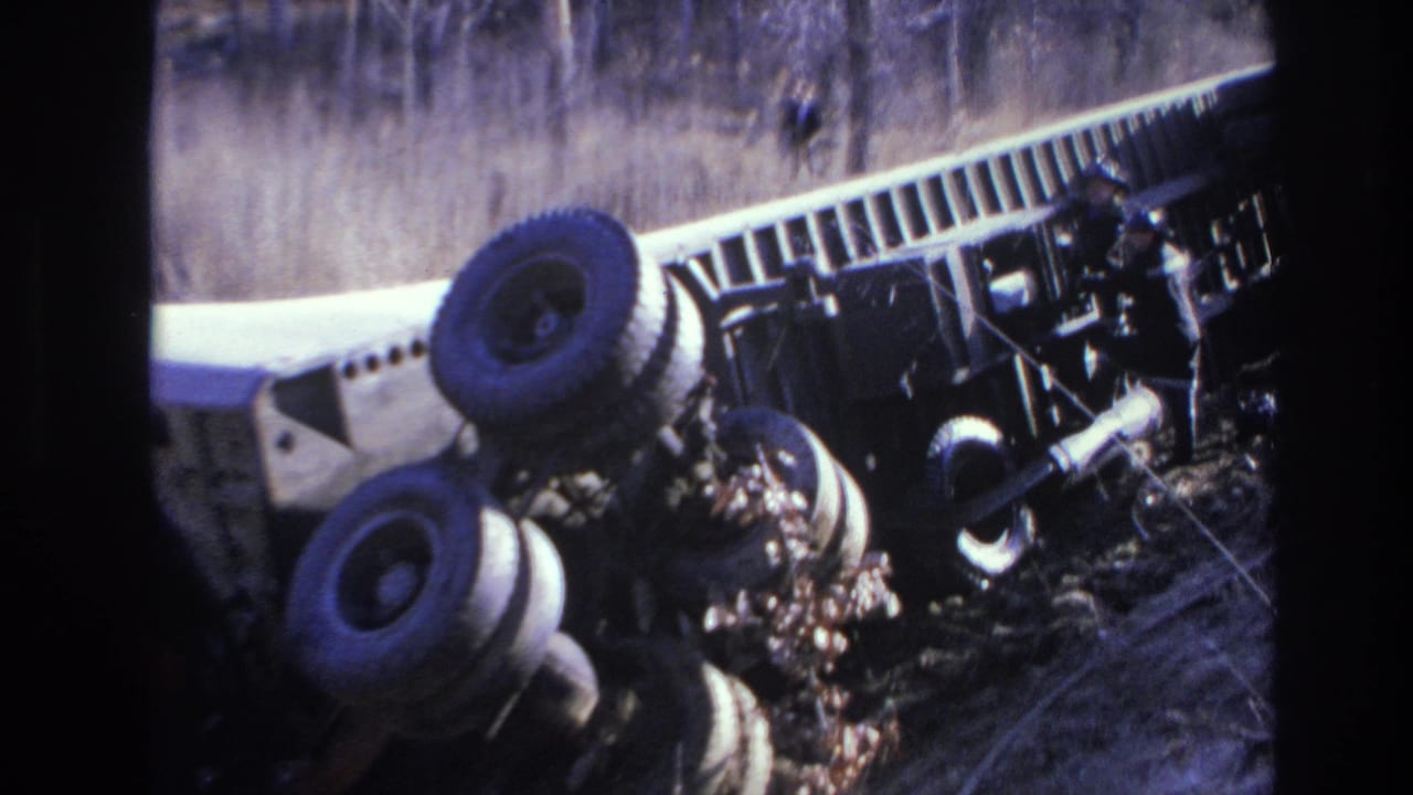 Overturned truck in brush with a responder near the wreckage and wheels facing upward.
