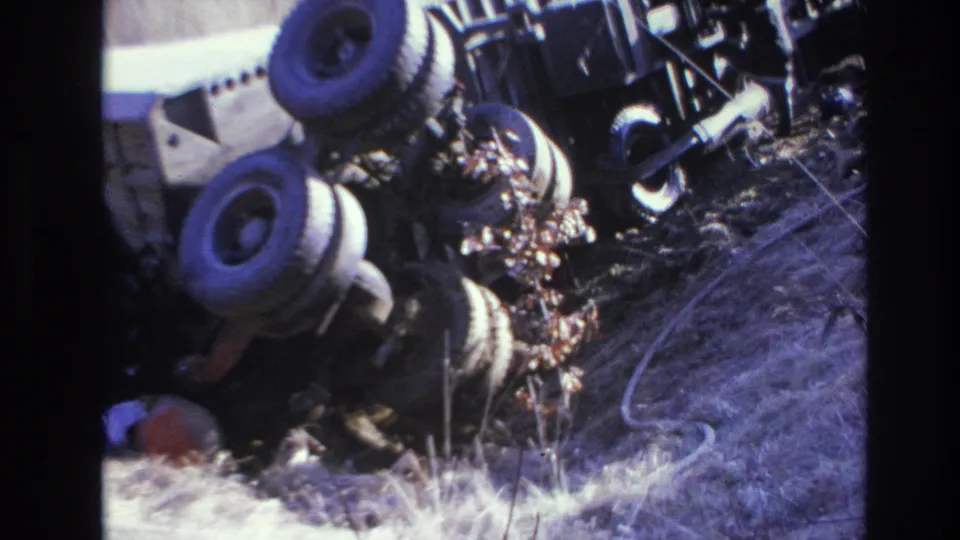 Handheld 8mm view of the truck wreck in Hoboken, with wheels, debris, and winter-bare grass visible.