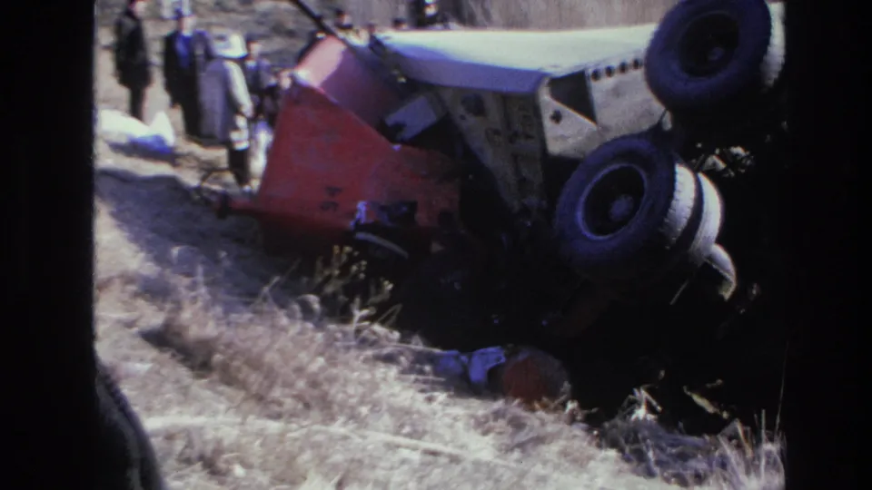 1966 Hoboken 8mm frame with onlookers or responders near the overturned truck in a grassy roadside ditch.