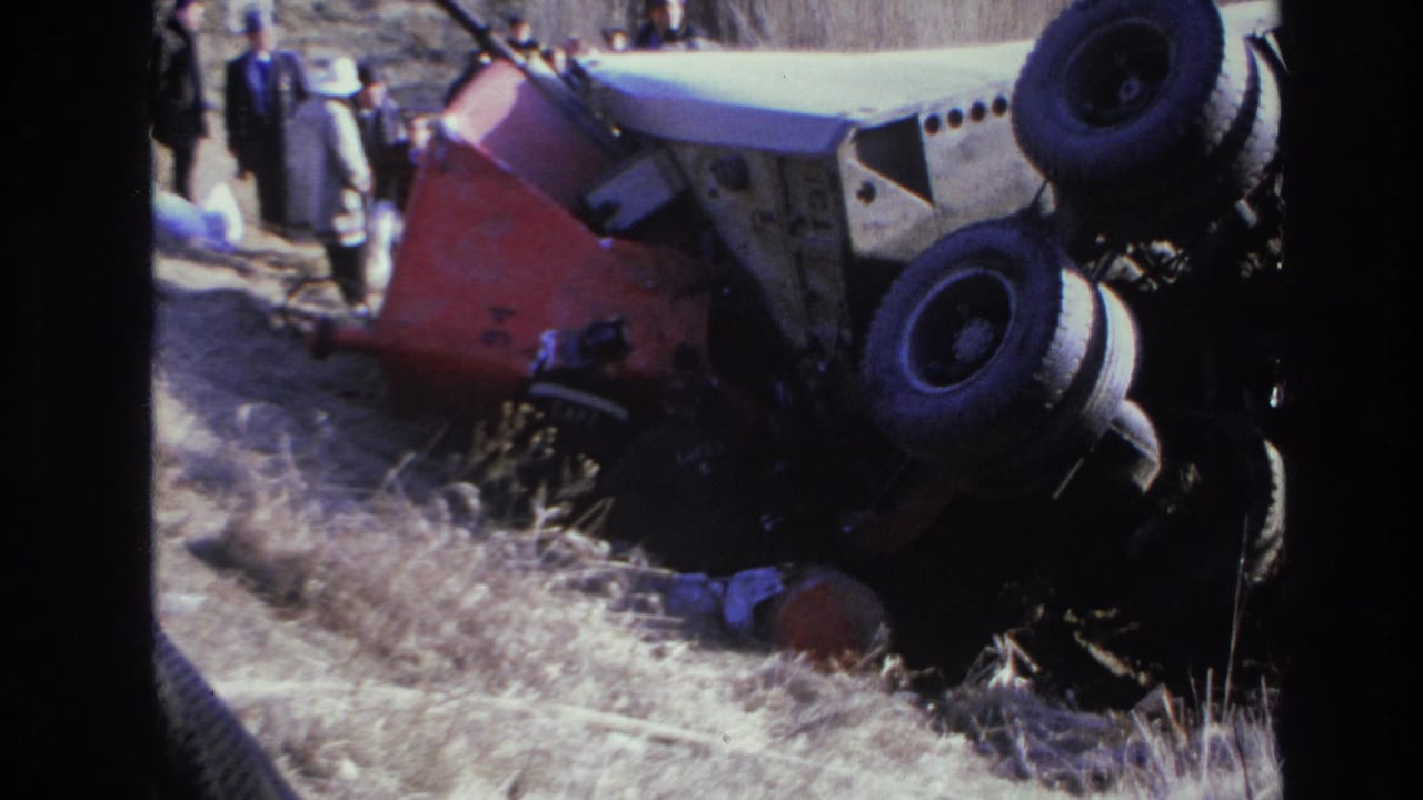 1966 Hoboken home-movie frame showing an overturned red and white car on a grassy embankment with people standing nearby.