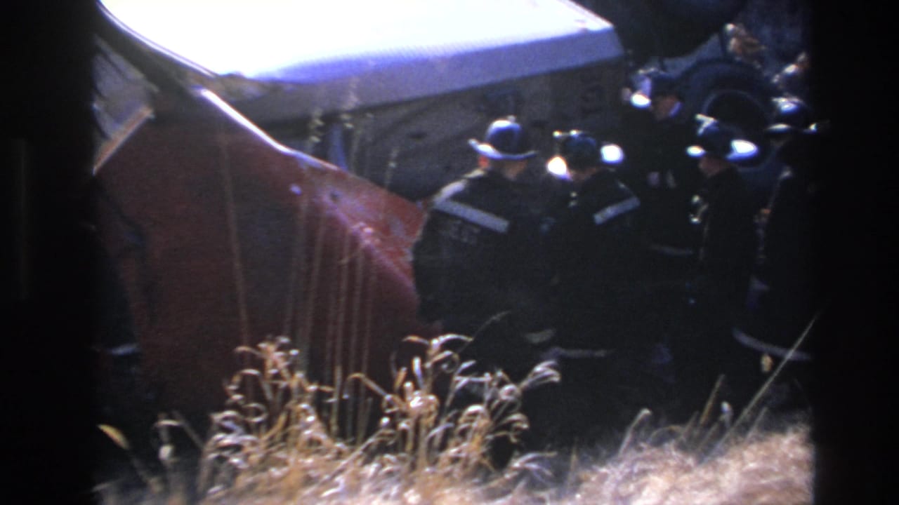 1966 Hoboken 8mm frame showing helmeted responders beside an overturned red vehicle under harsh night lighting.