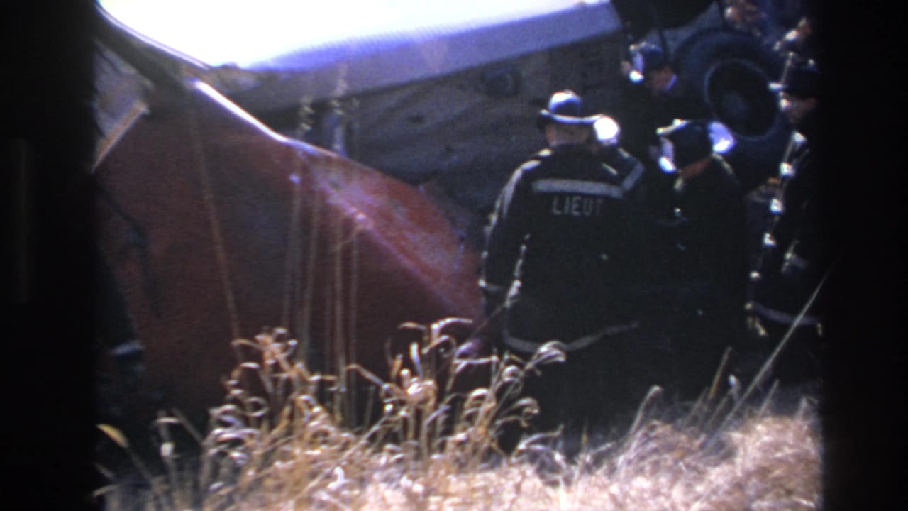 A responder with LIEUT lettering on the back faces the damaged vehicle at night.