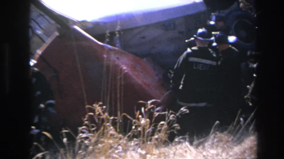 Helmeted responders in dark uniforms move around the overturned red vehicle in 1966 Hoboken night footage.