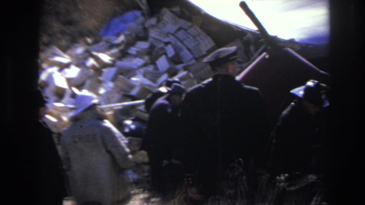 1966 Hoboken home-movie frame showing uniformed responders near scattered debris and a damaged red vehicle frame in daylight.