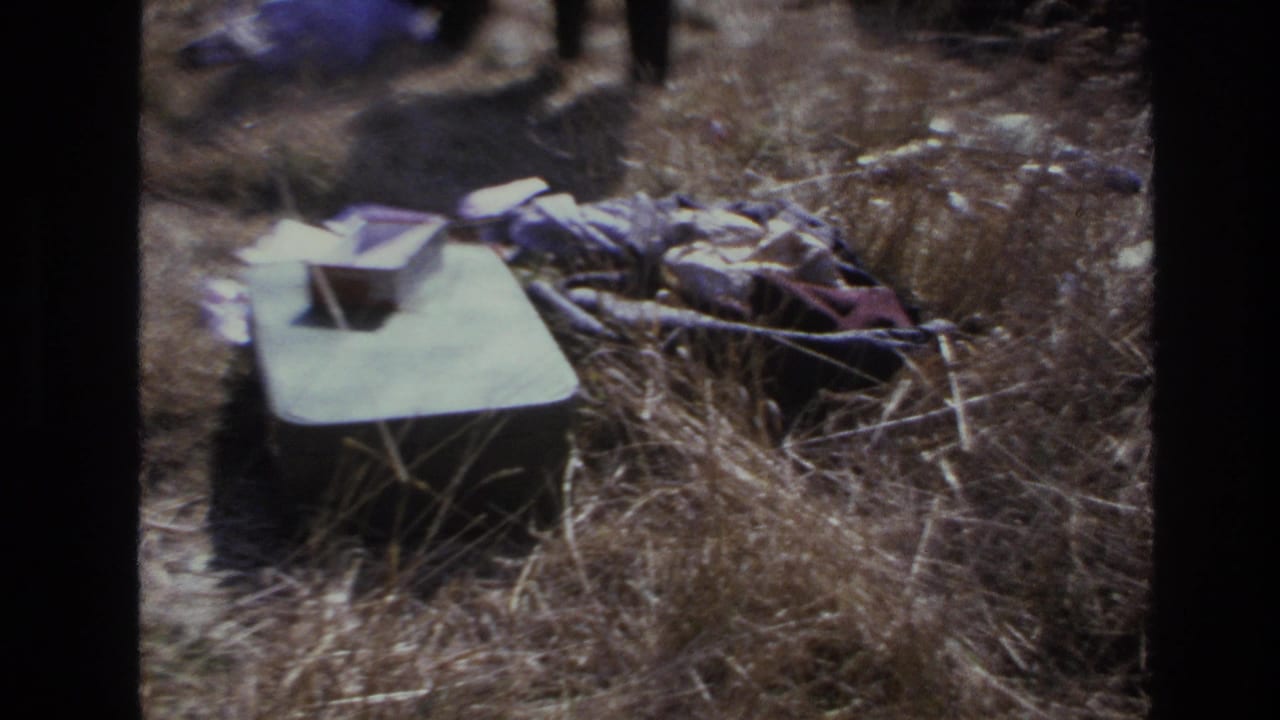 1966 Hoboken 8mm frame showing dry grass with crumpled fabric and a pale rectangular item on the ground.