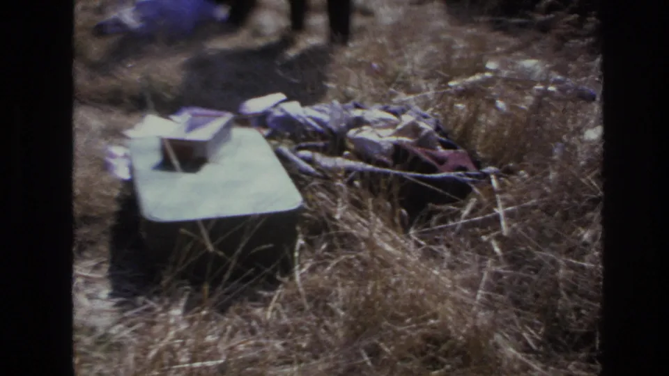 1966 Hoboken 8mm frame showing dry grass with crumpled fabric and a pale rectangular item on the ground.