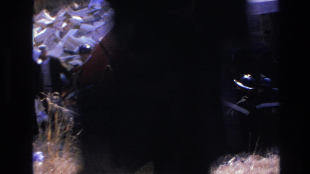 1966 Hoboken rescue scene with firefighters working beside an overturned red train car, seen through dark 8mm frame edges.