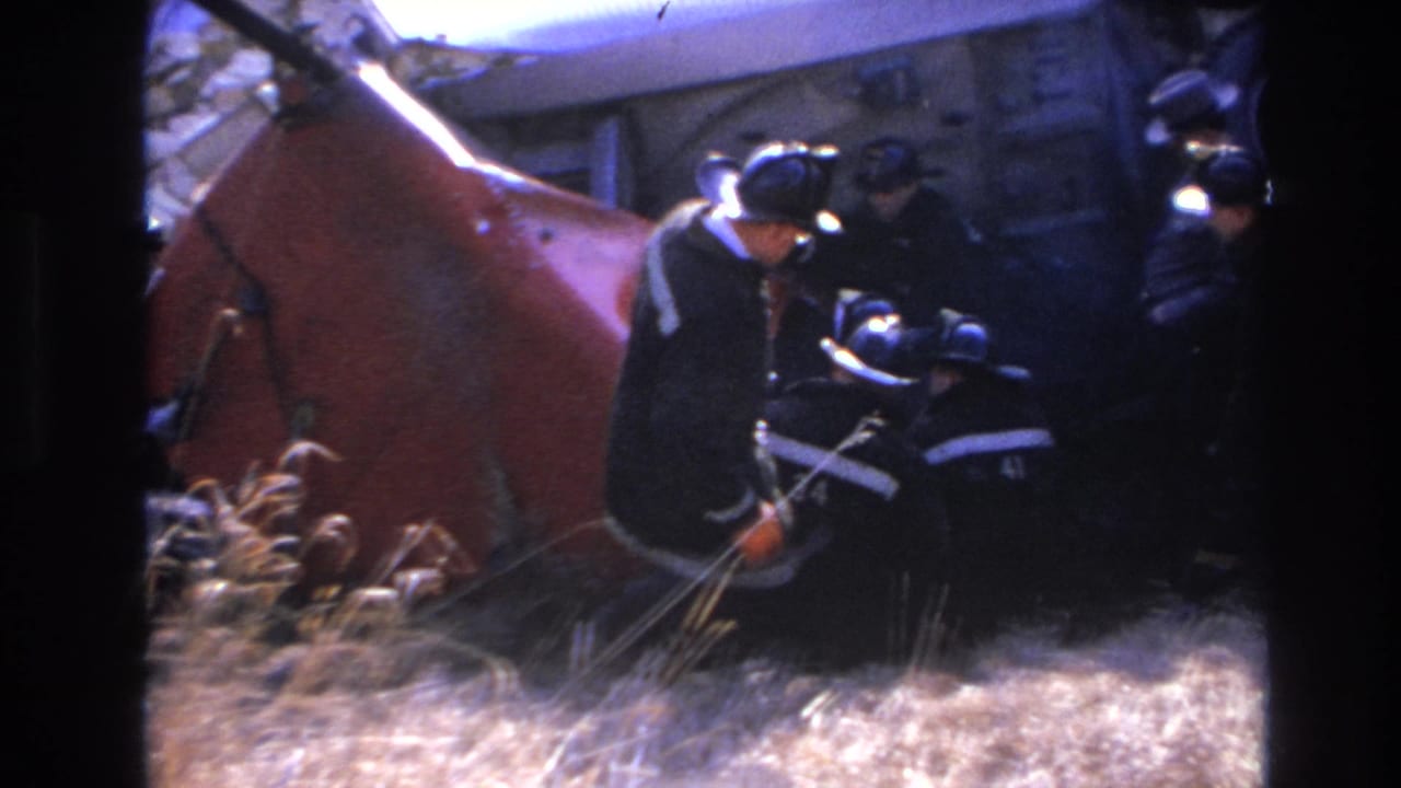 Several firefighters work beside a red overturned train car and visible wreckage.