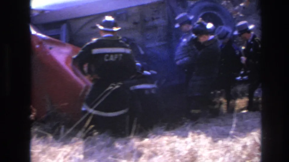 Firefighters continue rescue work near the overturned rail car, with a CAPT-marked jacket visible in the 1966 Hoboken footage.
