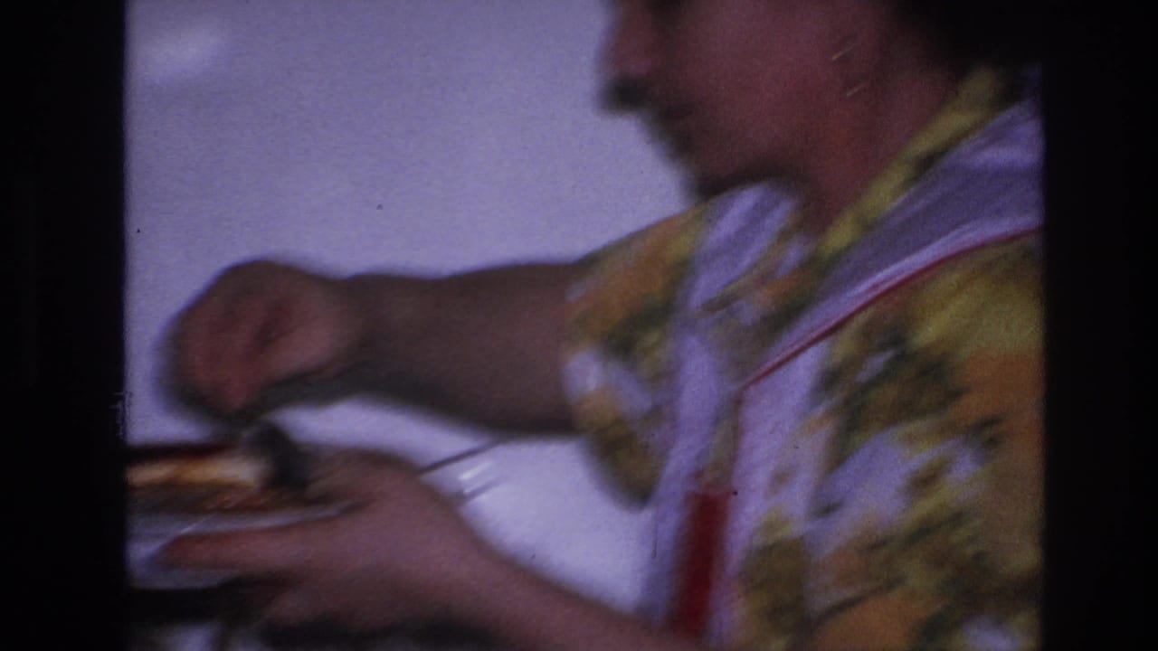 Blurred close view of a woman carrying a plate of food in a kitchen.