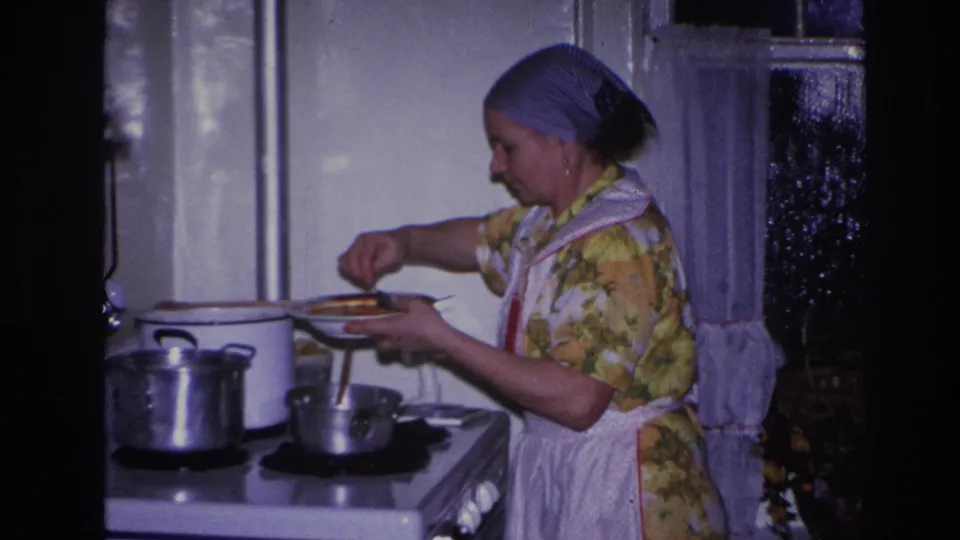 A wider 1966 Hoboken kitchen view shows the woman serving food near a white stove, metal pots, and a curtained window.