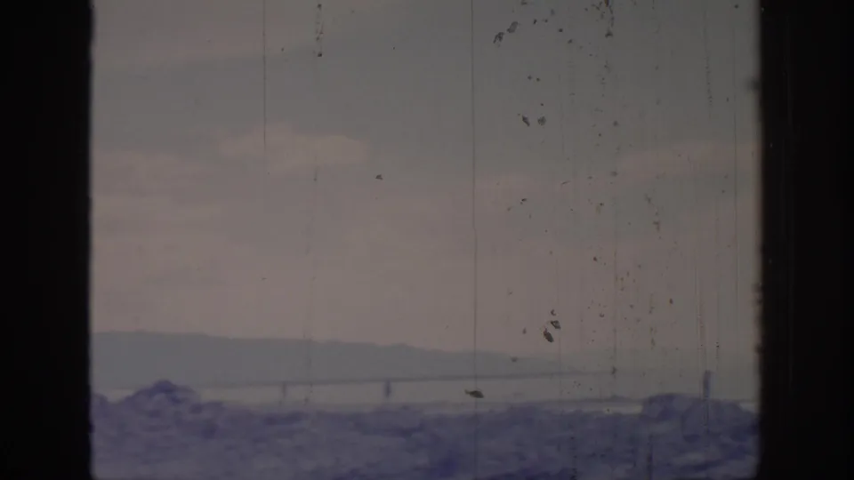 1966 8mm Sacramento-area home-movie view of cloudy sky, distant ridge, water, and dark window framing with visible film wear.