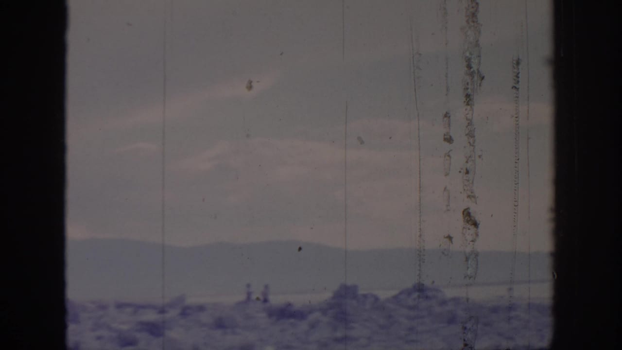 Window-framed 1966 8mm view toward distant mountains and water near Sacramento, with faint small figures or posts along the shoreline.