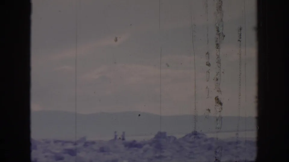 Window-framed 1966 8mm view toward distant mountains and water near Sacramento, with faint small figures or posts along the shoreline.