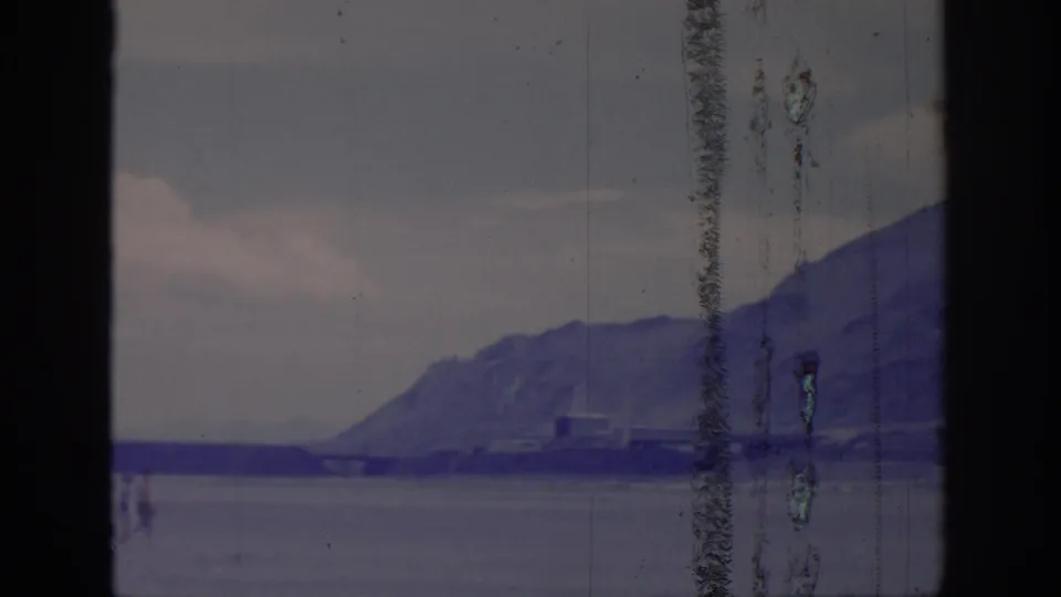 A closer 1966 8mm home-movie view shows a mountain above water with shoreline structures and heavy vertical film wear.
