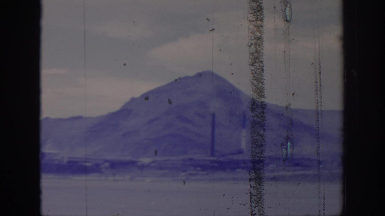 1966 8mm frame from Sacramento metadata showing a hazy mountain ridge with distant smokestacks, seen through dark vertical window framing.