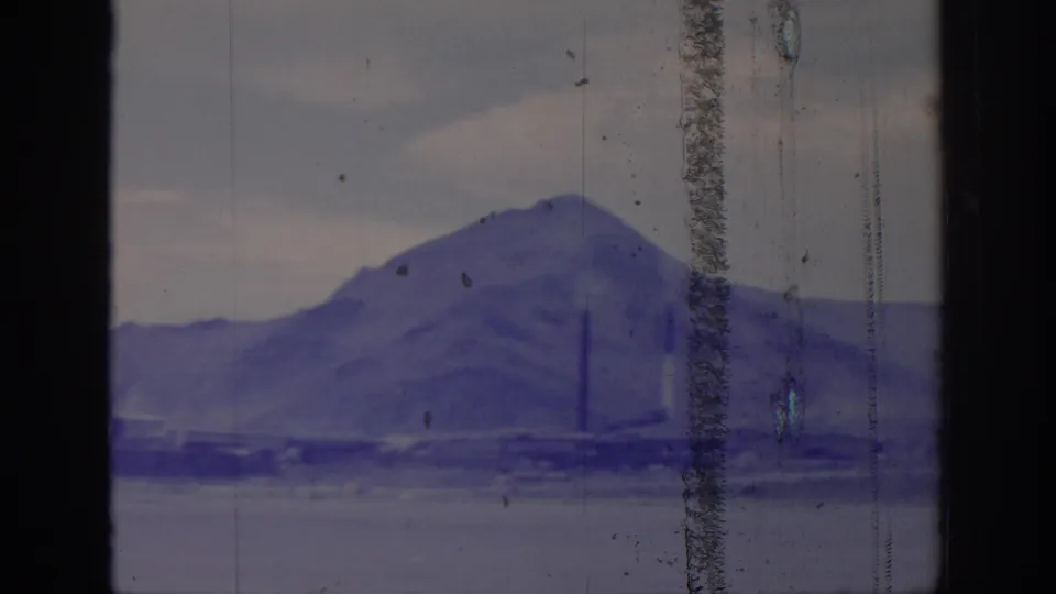 1966 8mm frame from Sacramento metadata showing a hazy mountain ridge with distant smokestacks, seen through dark vertical window framing.