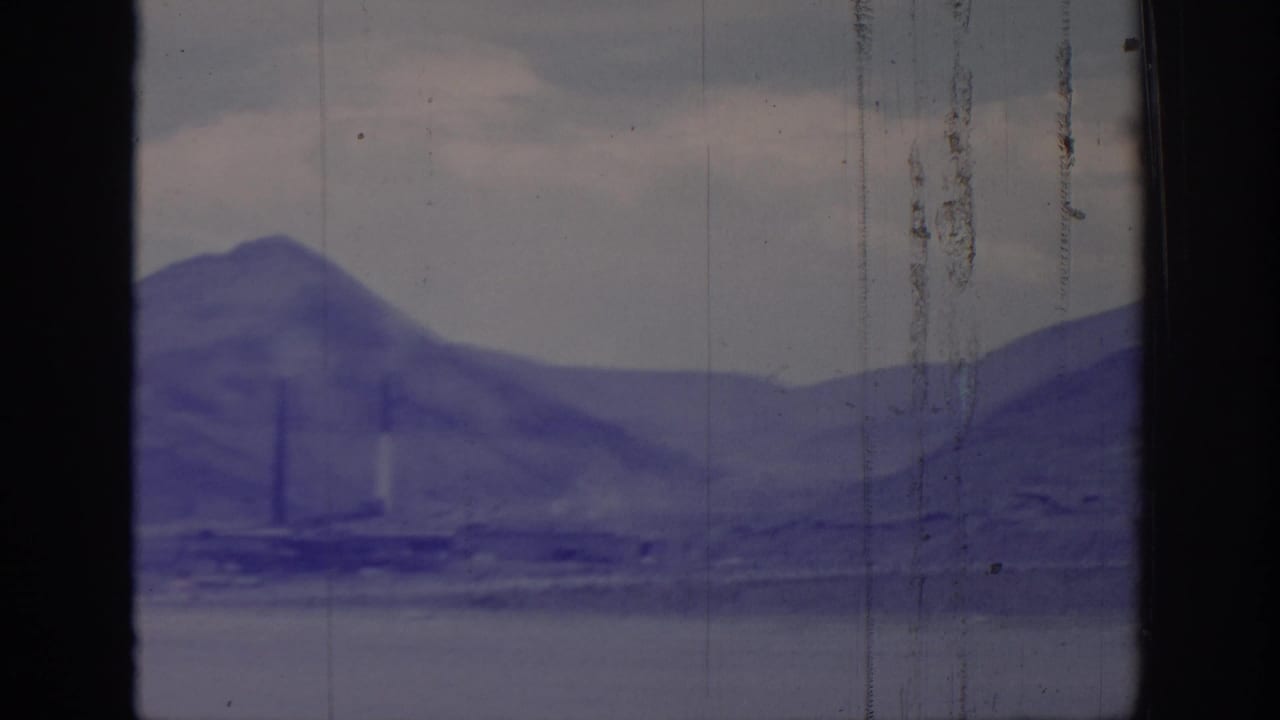 Blue-toned mountain peak with faint industrial structures below and film scratches.