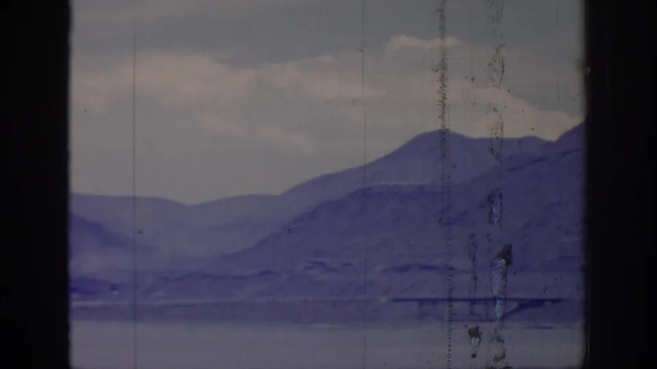 1966 Sacramento-context 8mm frame showing layered mountain ridges beneath a cloudy sky, with window framing and heavy film wear visible.