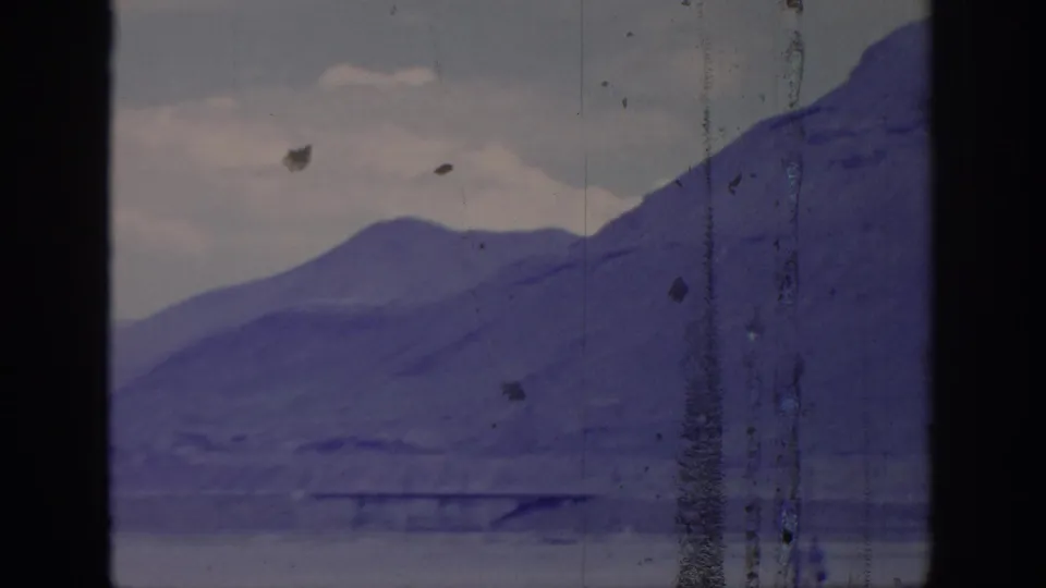 Purple-shifted 8mm frame showing a hazy mountain slope and low foreground, bordered by dark window framing and vertical film scratches.