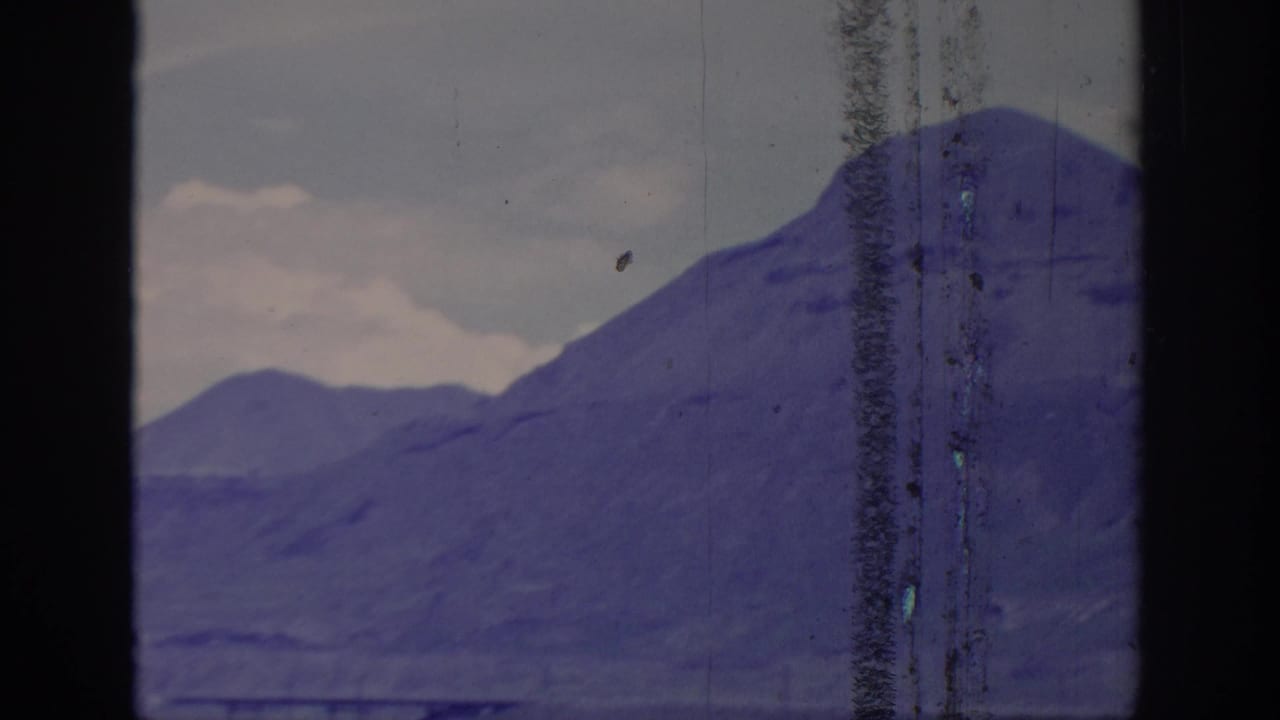 1966 8mm frame showing distant mountain ridges through a dark window or vehicle frame, with aged color shift and scratches.