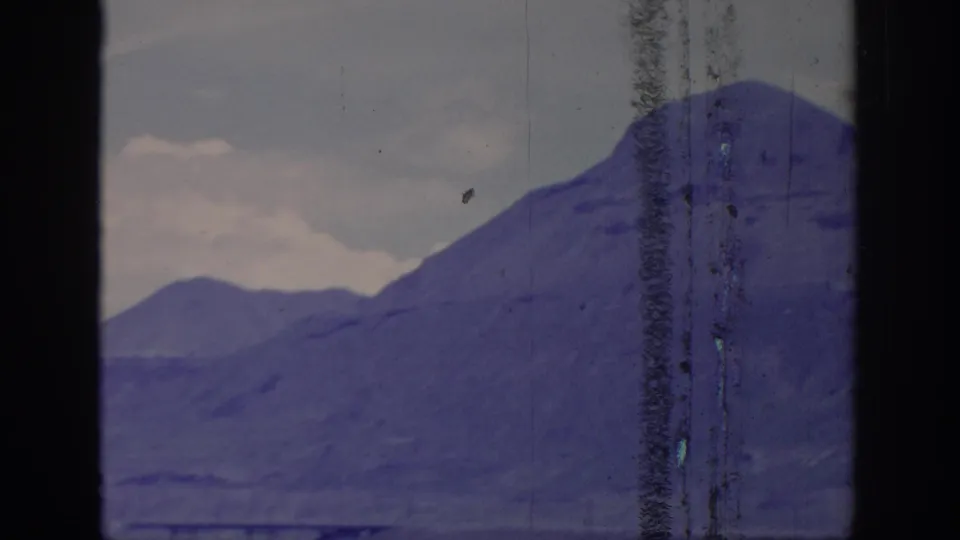 1966 8mm frame showing distant mountain ridges through a dark window or vehicle frame, with aged color shift and scratches.