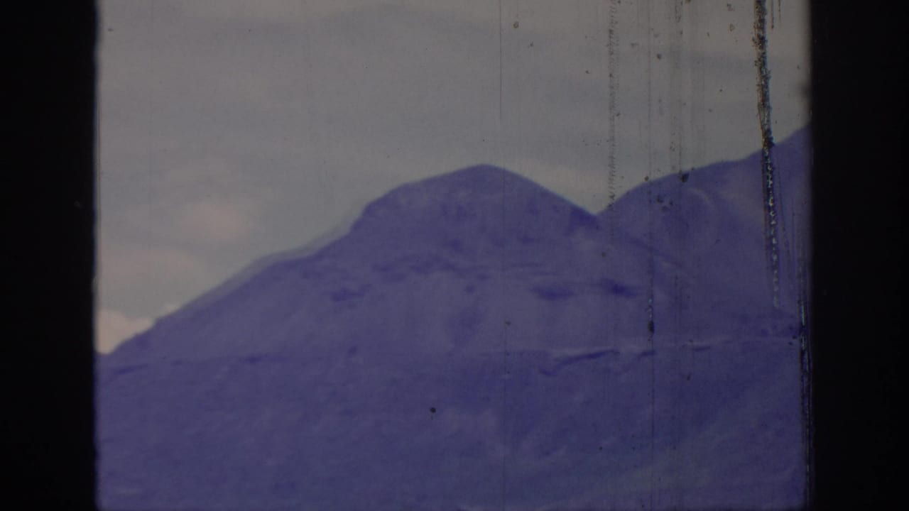 1966 8mm view of a broad mountain slope seen through a dark frame division, with visible film wear and purple aging.